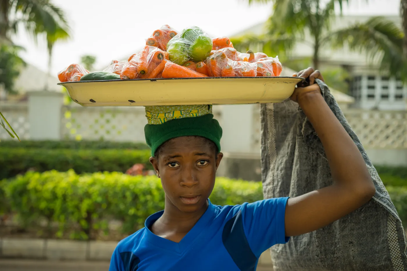 A young vendor carrying a tray of fresh vegetables on her head in Abuja, Nigeria